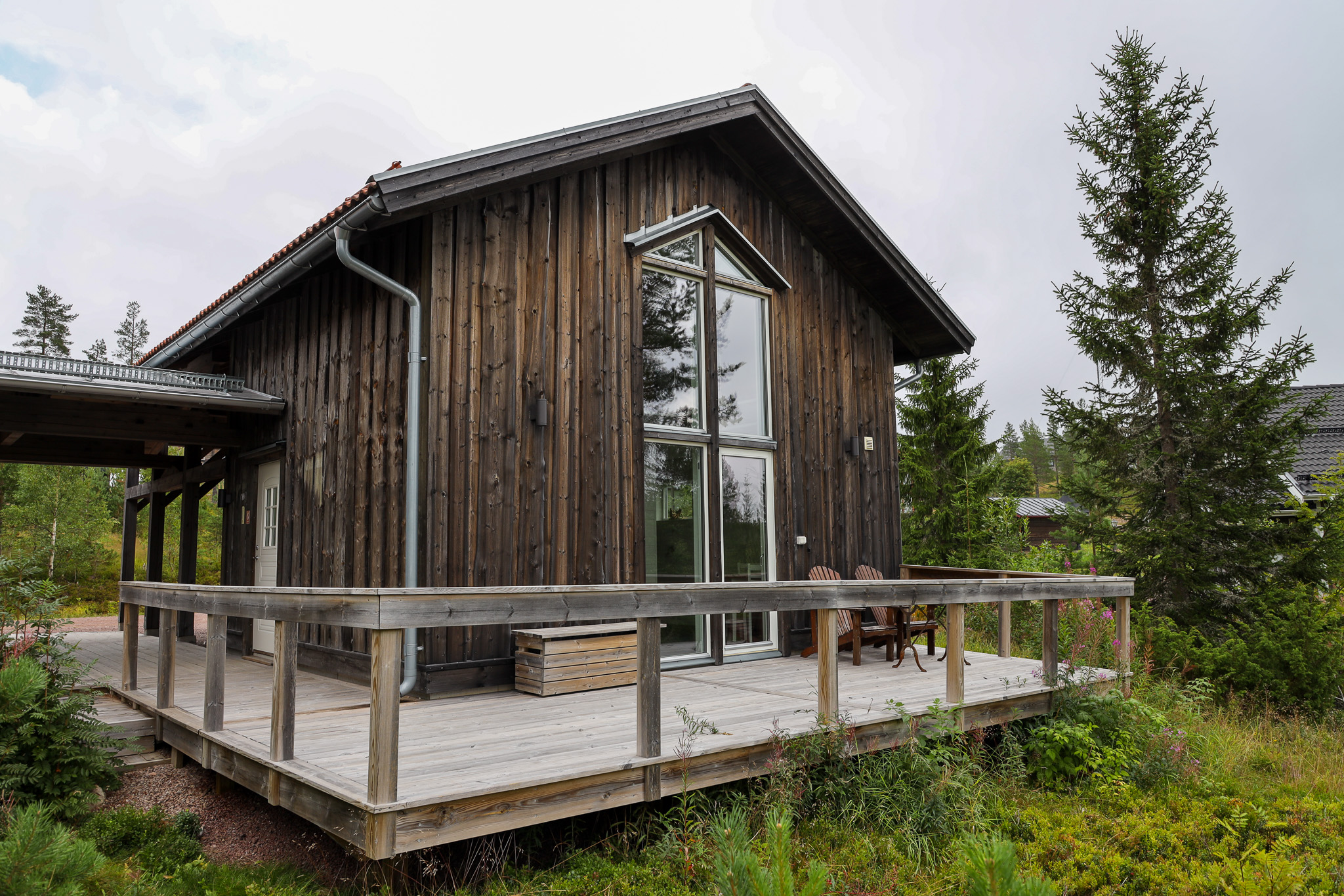 En modern mörk trästuga med stora fönster och altan, omgiven av grönska och träd. En modern mörk trästuga med stora fönster och altan, omgiven av grönska och träd.