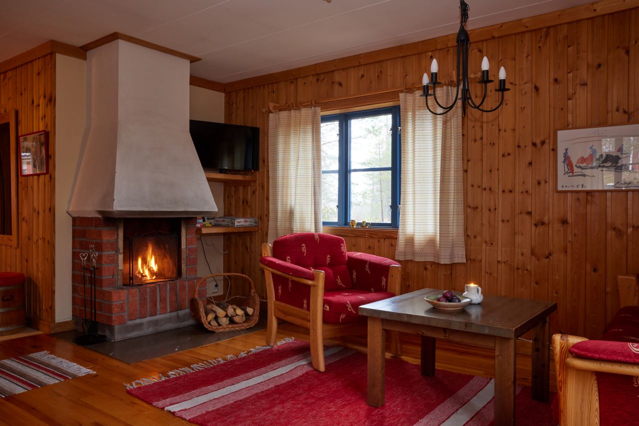 Ett mysigt vardagsrum med träväggar, öppen spis, röda fåtöljer och ett träbord på en matta.