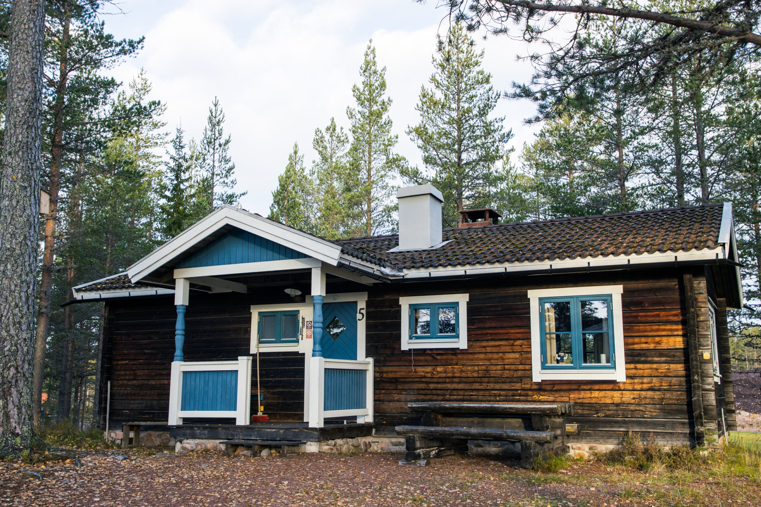 Trästuga med blå dörr och fönster, omgiven av skog.