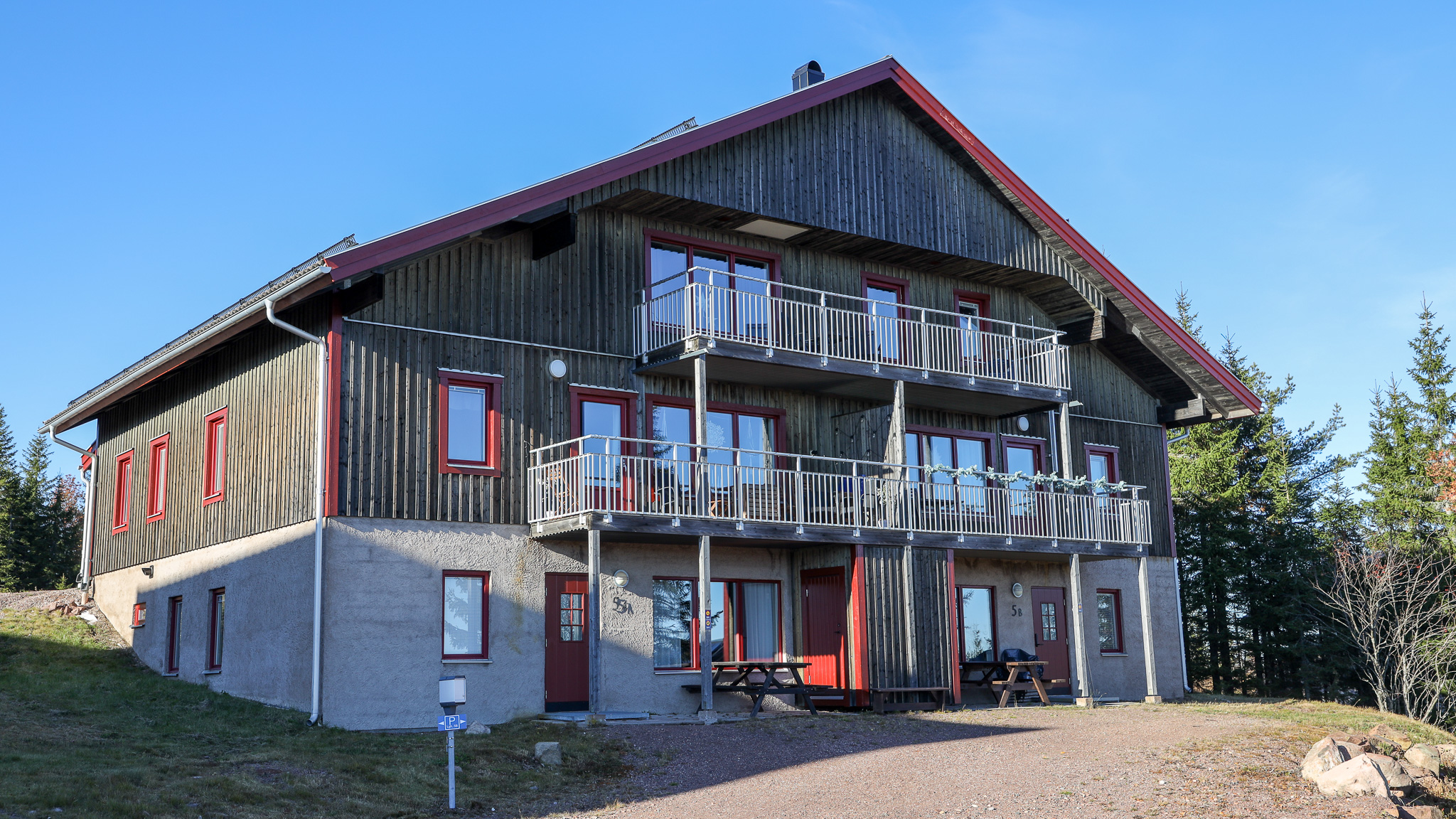 Större byggnad i flera våningar med balkonger och fasad i ljus puts och trä, belägen i ett öppet område med klar himmel. Större byggnad i flera våningar med balkonger och fasad i ljus puts och trä, belägen i ett öppet område med klar himmel.