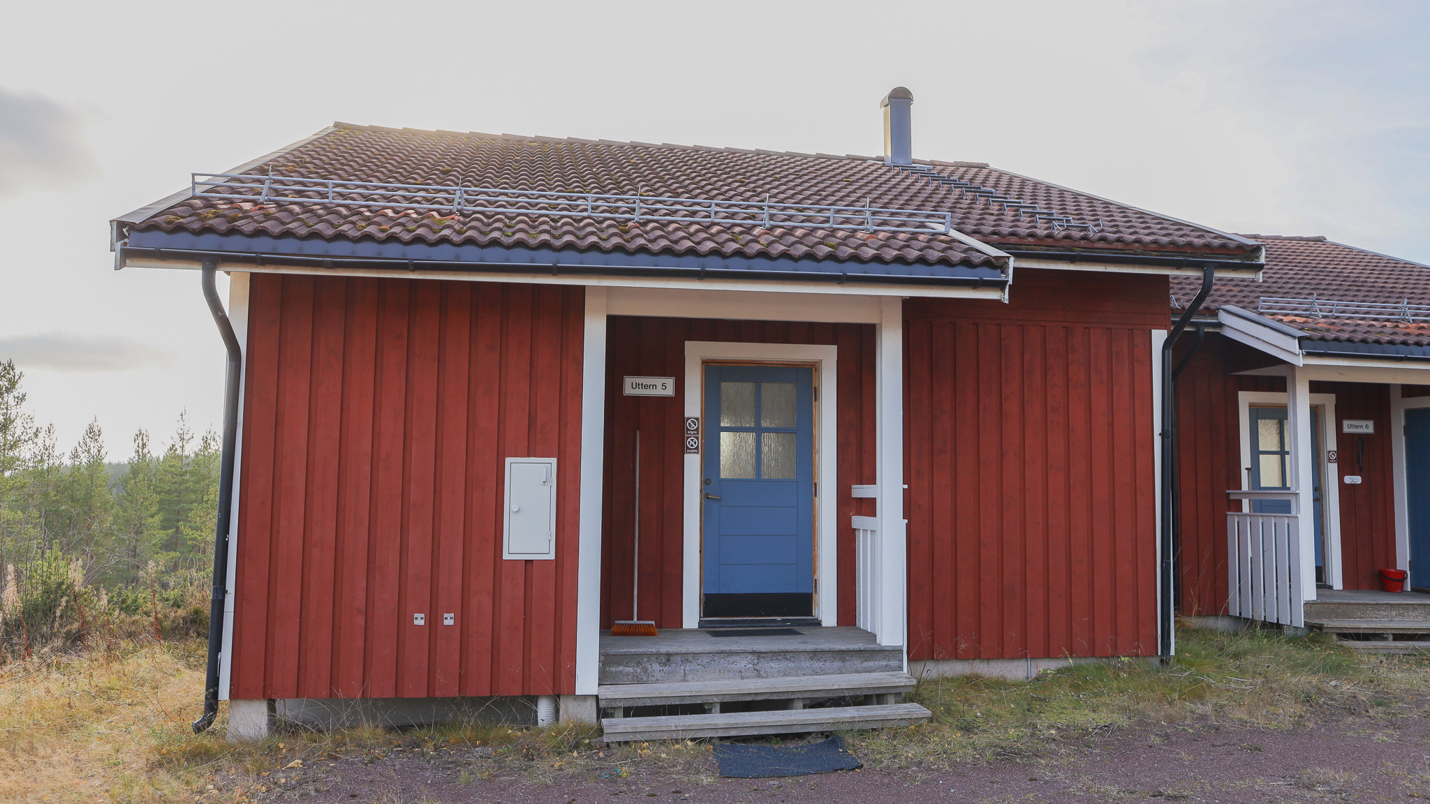 Röd enplansstuga med vita knutar, entré med liten farstukvist och grusad mark runt huset. Röd enplansstuga med vita knutar, entré med liten farstukvist och grusad mark runt huset.