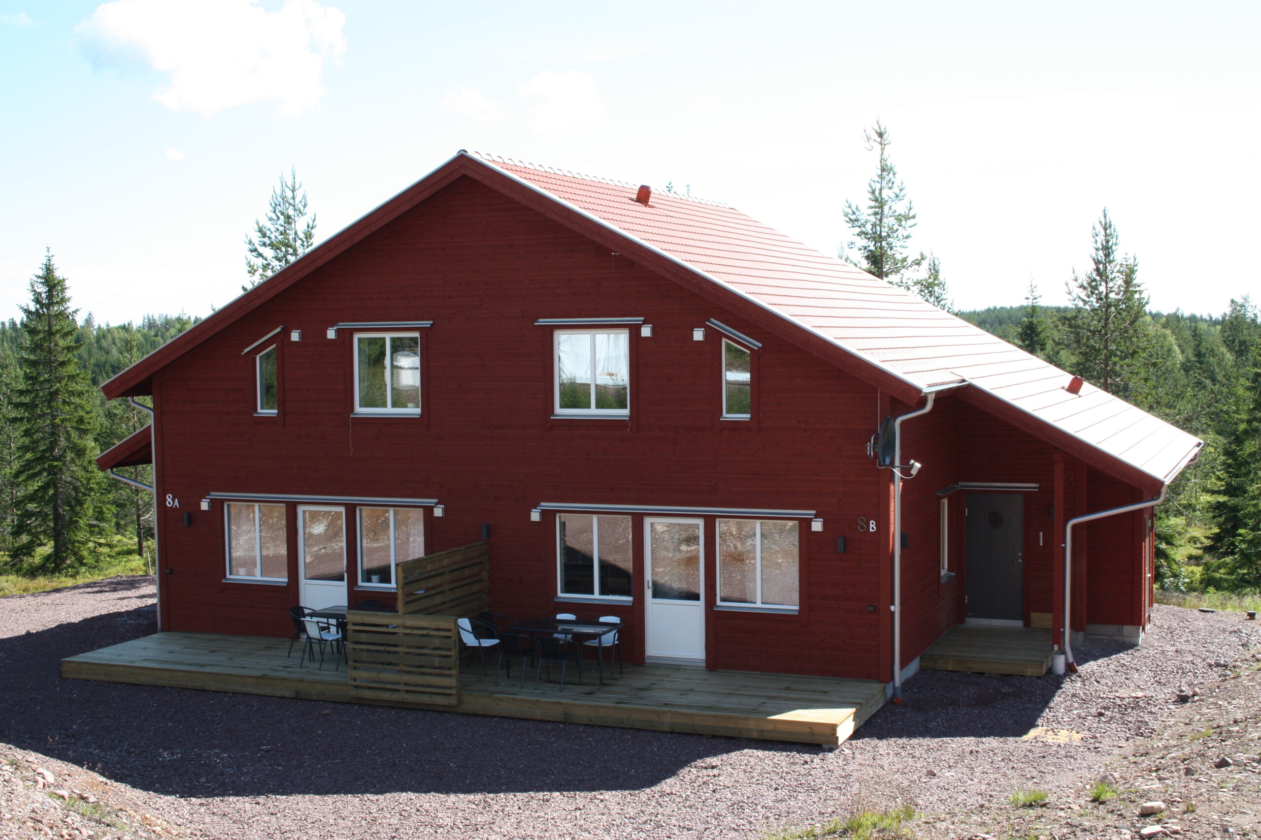 Röd byggnad i två våningar med flera fönster och parkeringsyta framför.