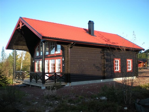 Trästuga med rött tak och stora fönster, omgiven av träd och natur. Trästuga med rött tak och stora fönster, omgiven av träd och natur.