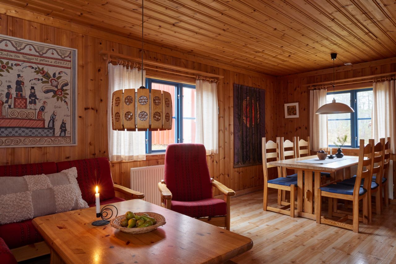 Vardagsrum med soffa, fåtöljer, soffbord och matplats i träklädd interiör.