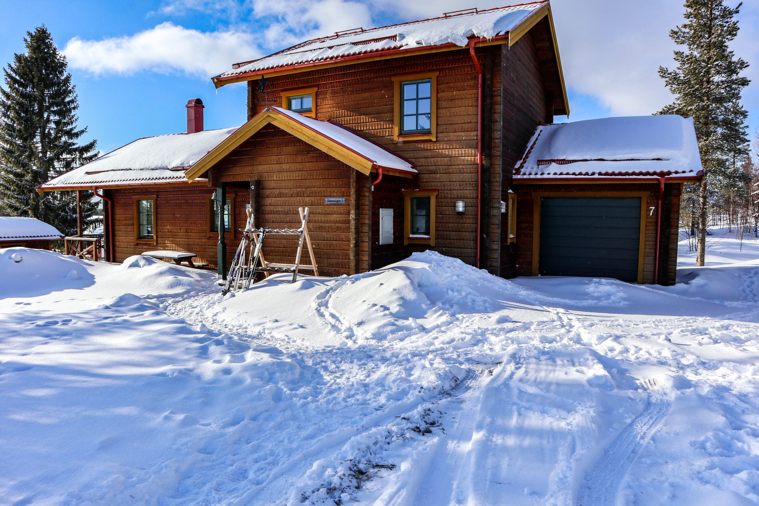 Trästuga i två våningar med garage och snö på marken.