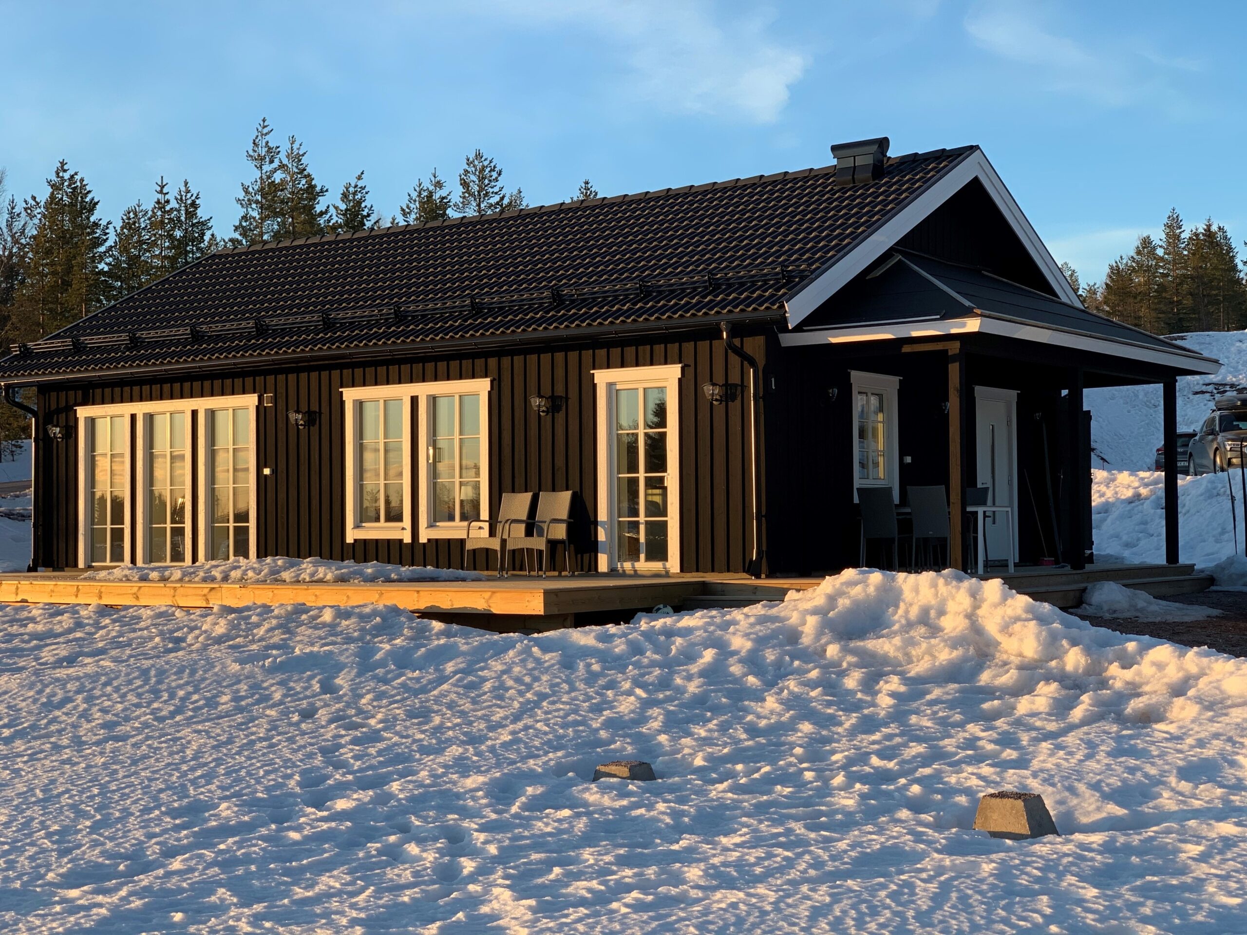 Mörk trästuga med stora fönster i snötäckt landskap.