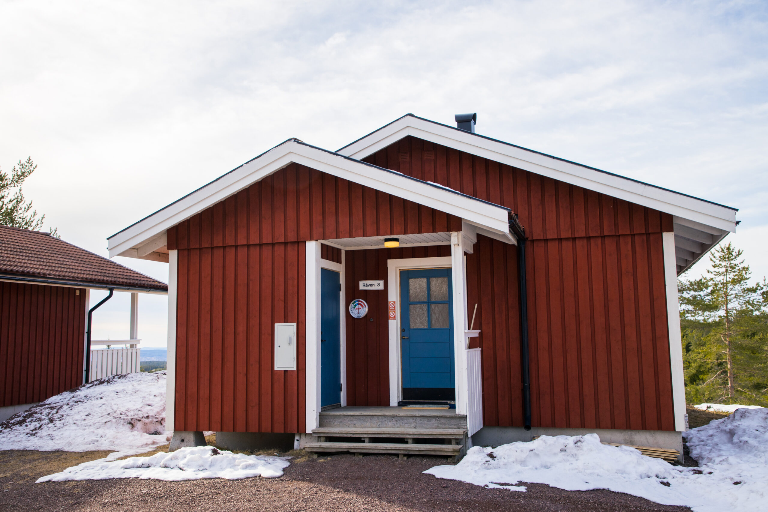 Röd stuga med entré, liten veranda och snötäckt mark.