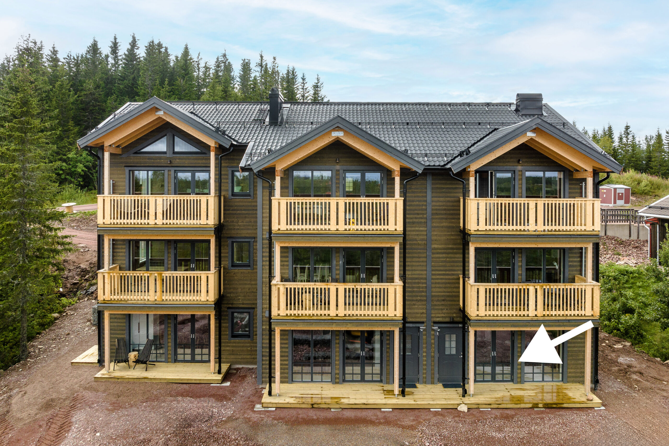 Flerbostadshus i trä med balkonger och entré på markplan.