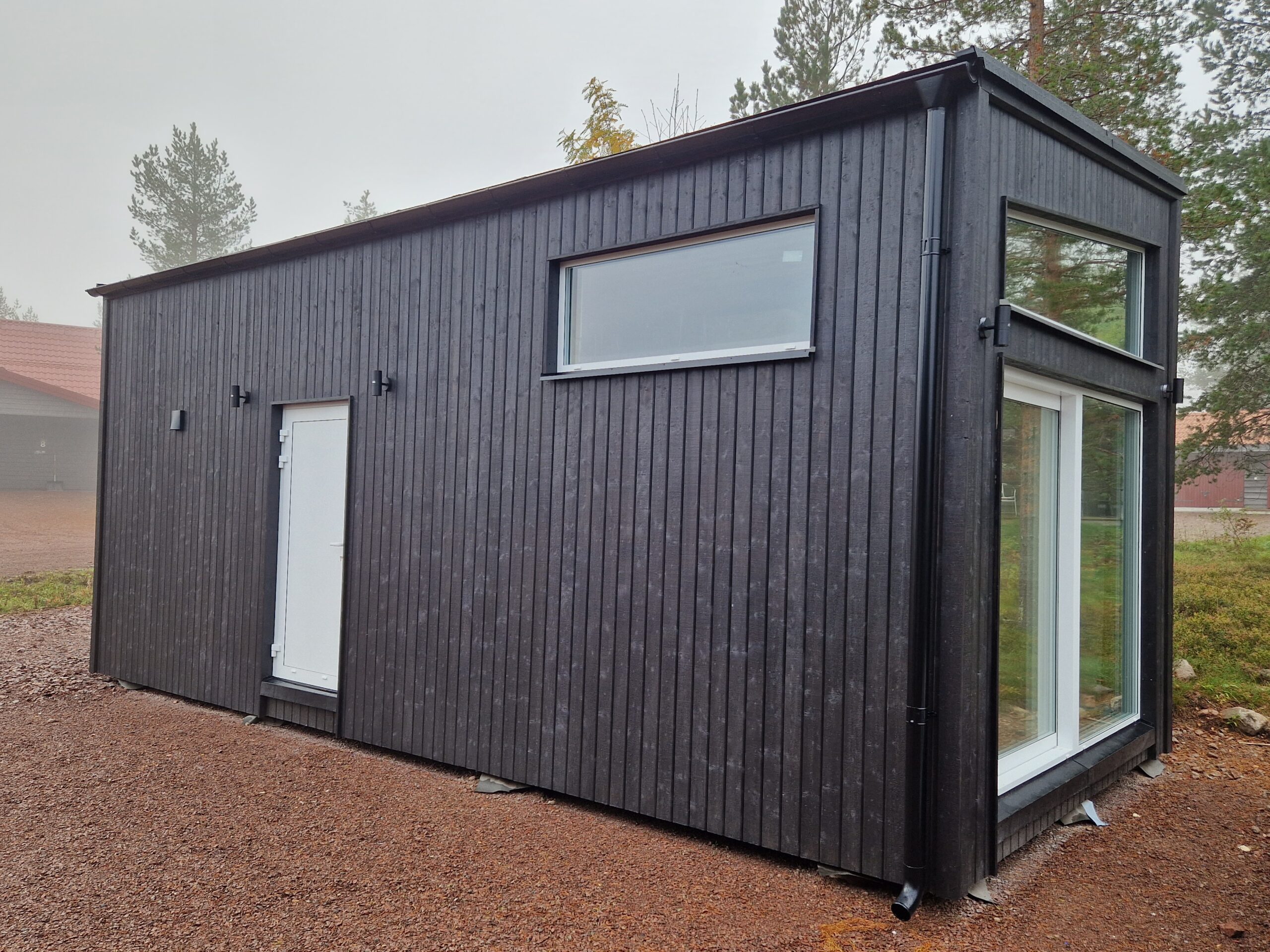 Mörk byggnad med stora fönster och grusyta runt byggnaden. Mörk byggnad med stora fönster och grusyta runt byggnaden.