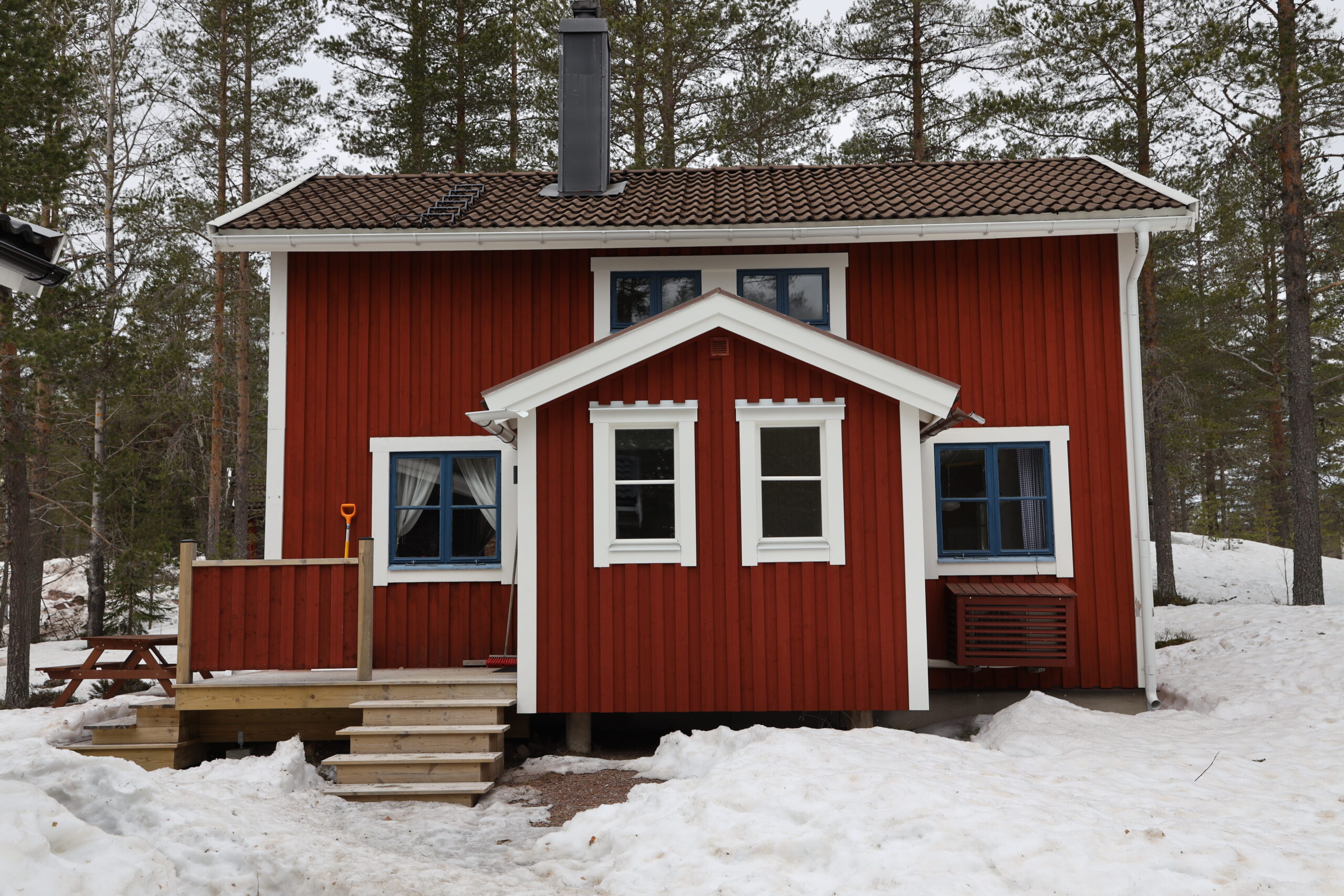 Röd stuga med entré och trappa i snötäckt skogsmiljö. Röd stuga med entré och trappa i snötäckt skogsmiljö.