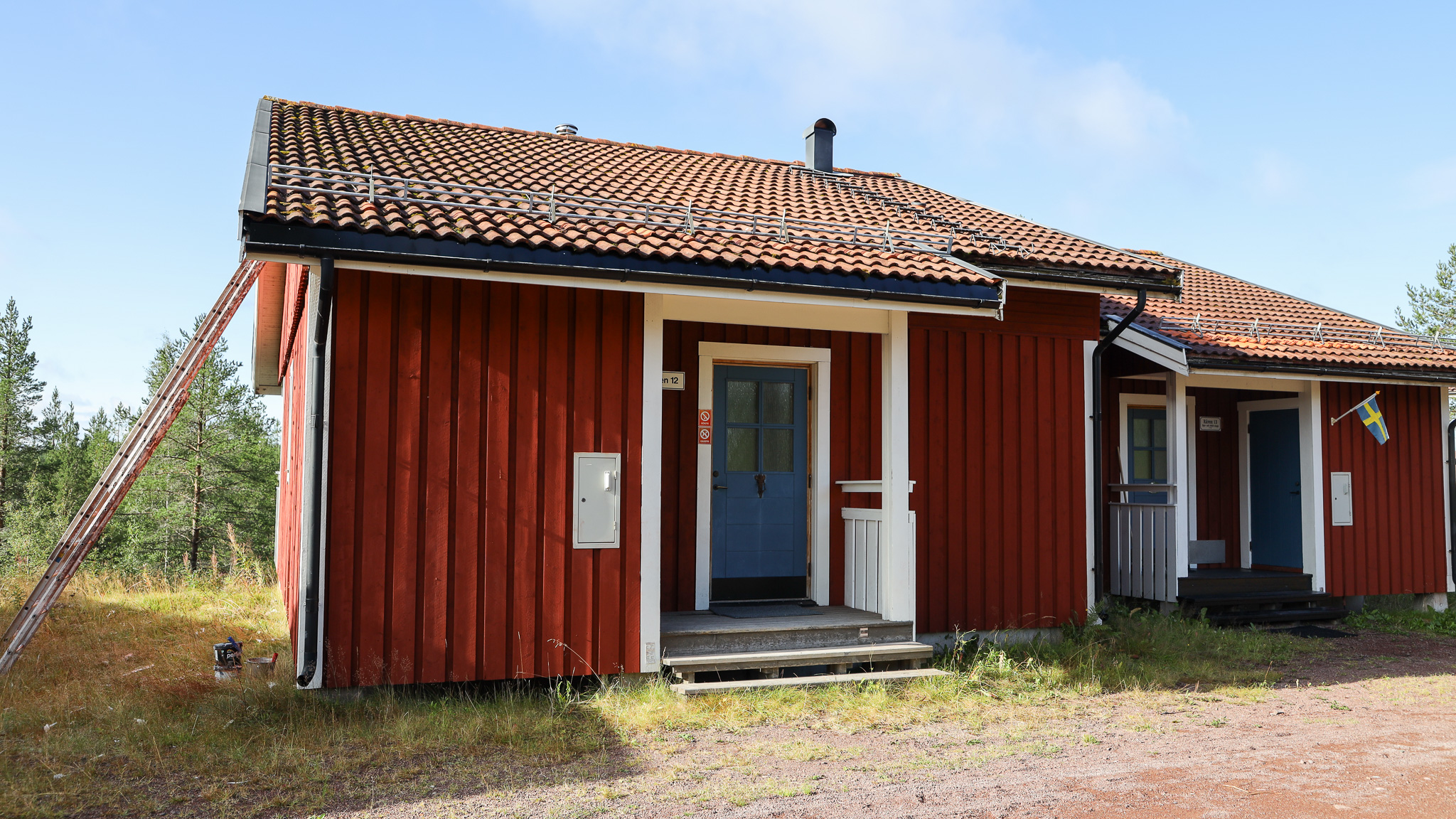 Röd stuga med entré, vita detaljer och gräsyta framför. Röd stuga med entré, vita detaljer och gräsyta framför.