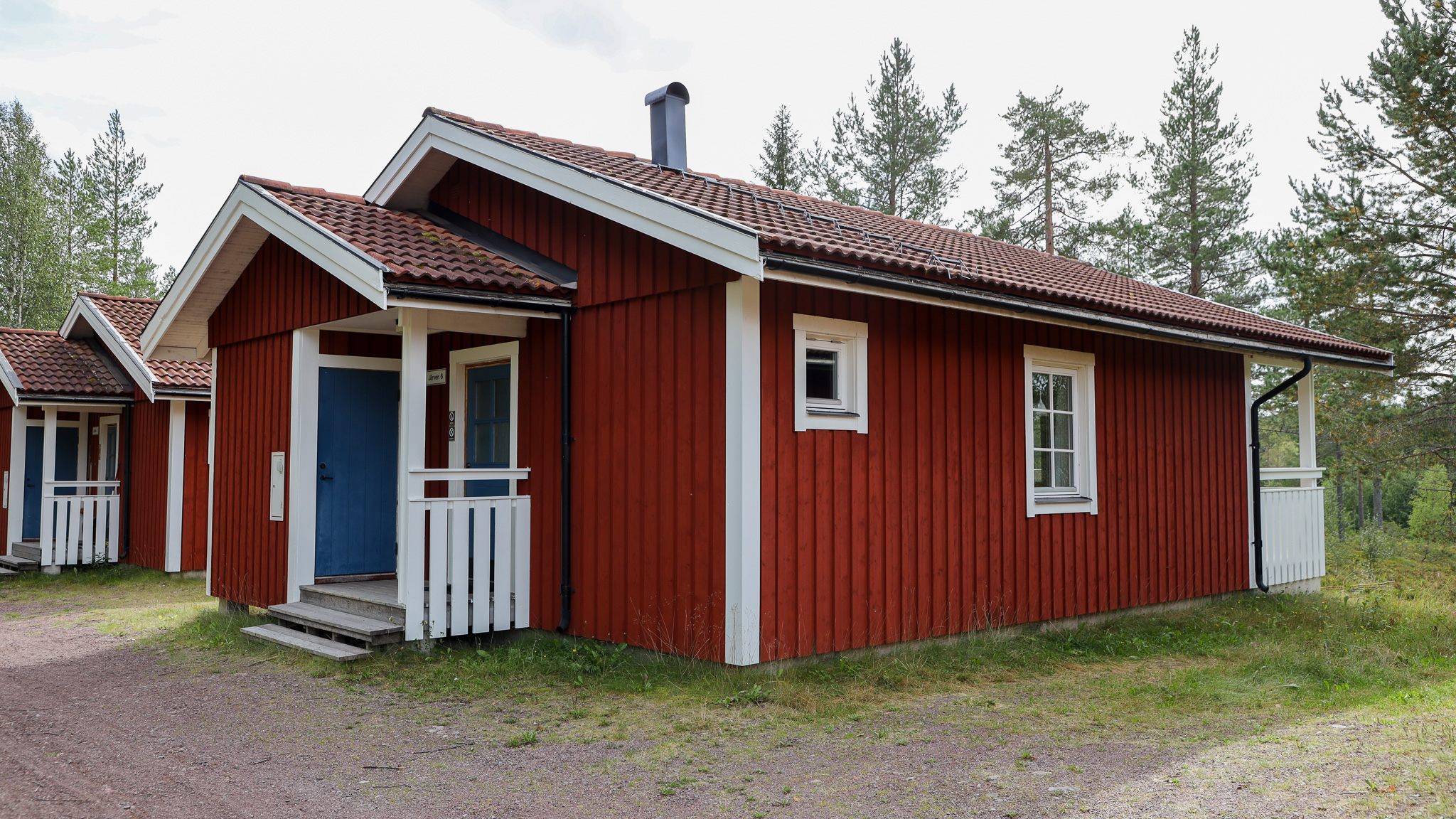 Röd stuga med entré, vita detaljer och gräsyta framför. Röd stuga med entré, vita detaljer och gräsyta framför.