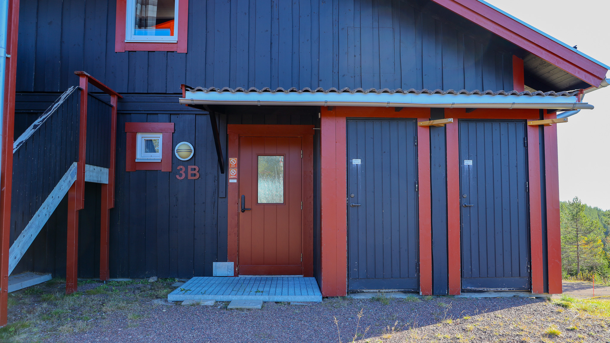 Mörk träbyggnad med entrédörr, garageportar och utvändig trappa. Mörk träbyggnad med entrédörr, garageportar och utvändig trappa.