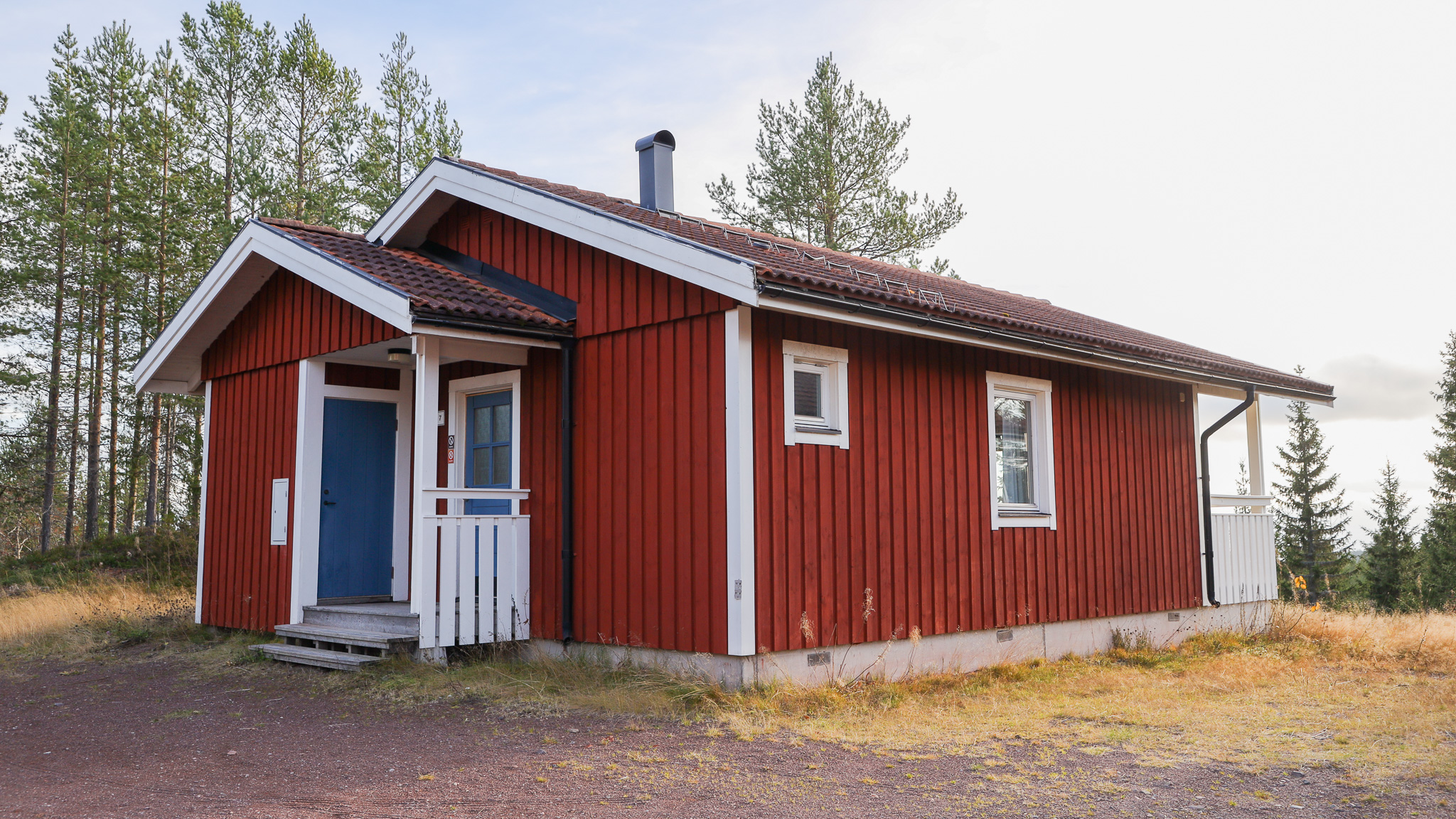 Röd stuga med entré, vita detaljer och gräsyta framför. Röd stuga med entré, vita detaljer och gräsyta framför.