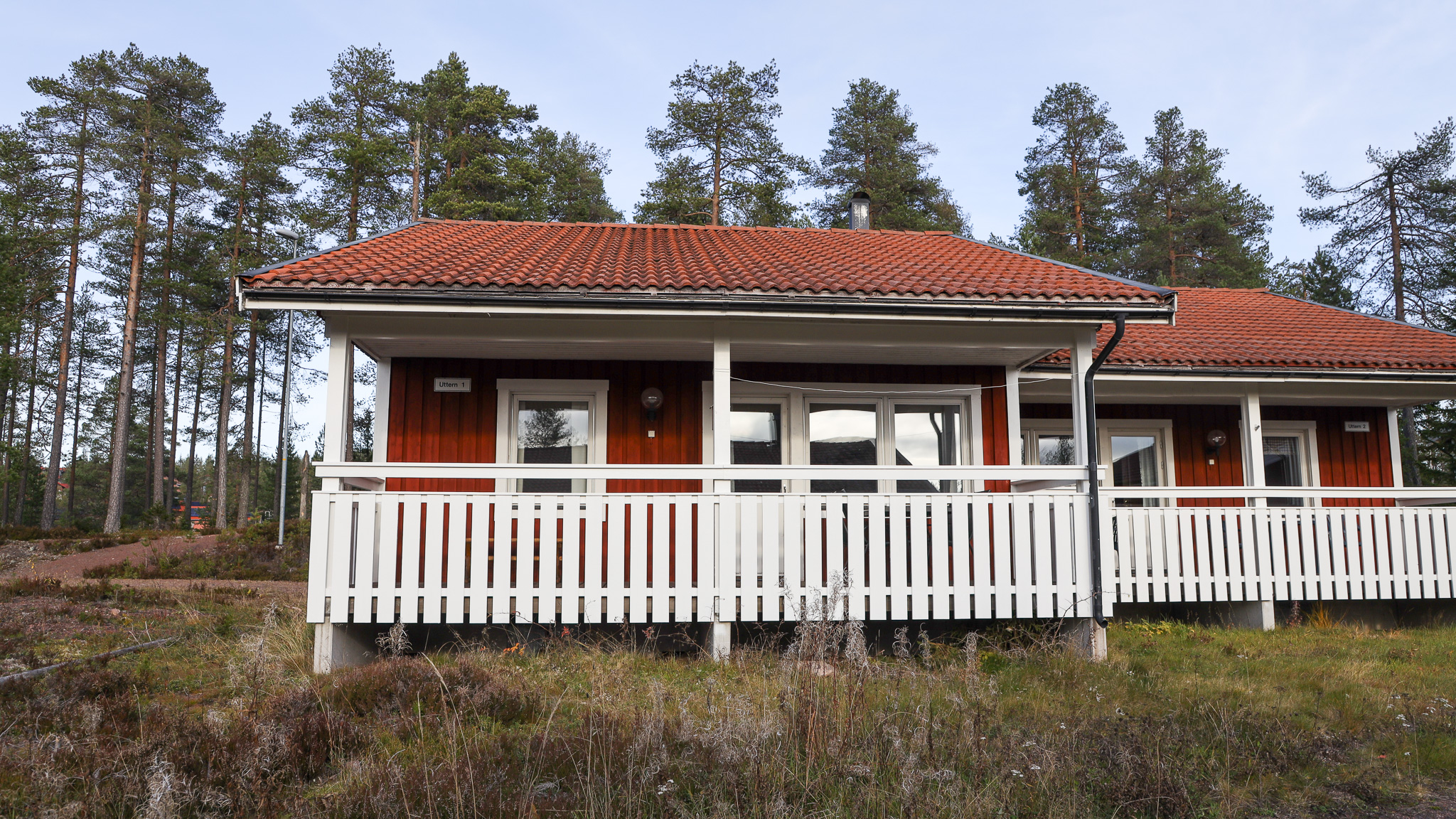 Enplansstuga med veranda och vita räcken omgiven av träd. Enplansstuga med veranda och vita räcken omgiven av träd.
