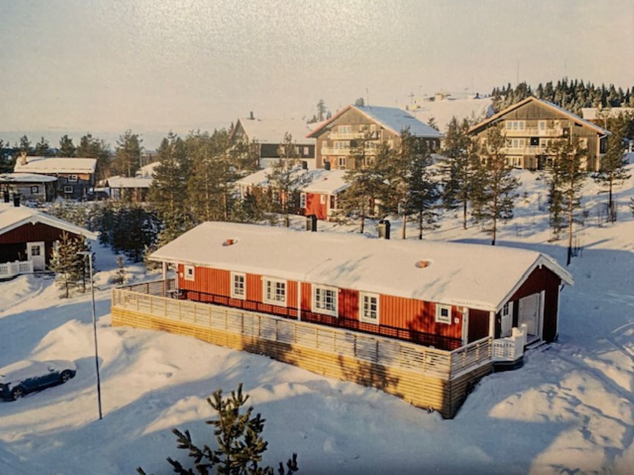 Flygbild över lång byggnad i snötäckt område med omgivande hus och träd. Flygbild över lång byggnad i snötäckt område med omgivande hus och träd.
