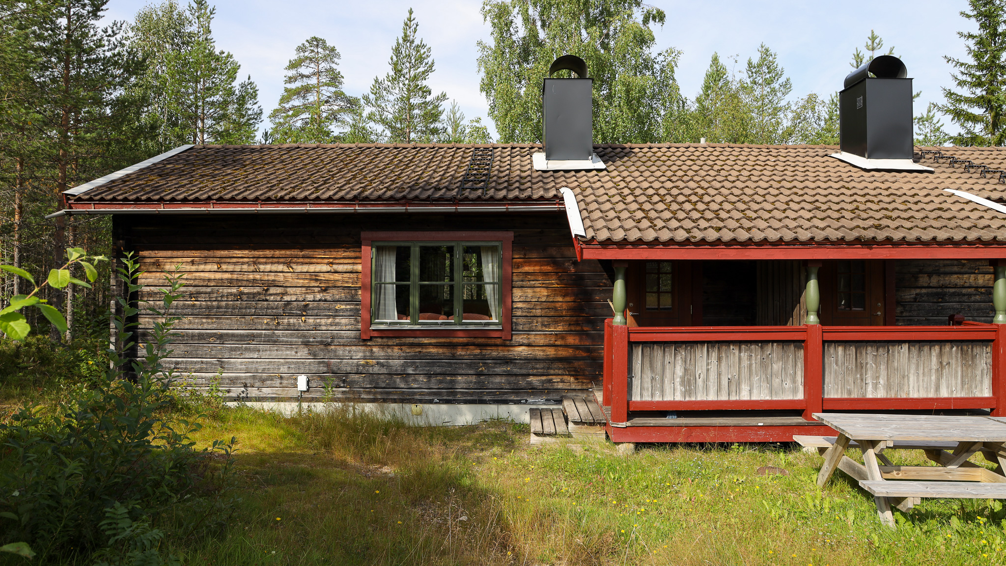 Mörk trästuga med veranda, omgiven av skog och grönska. Mörk trästuga med veranda, omgiven av skog och grönska.