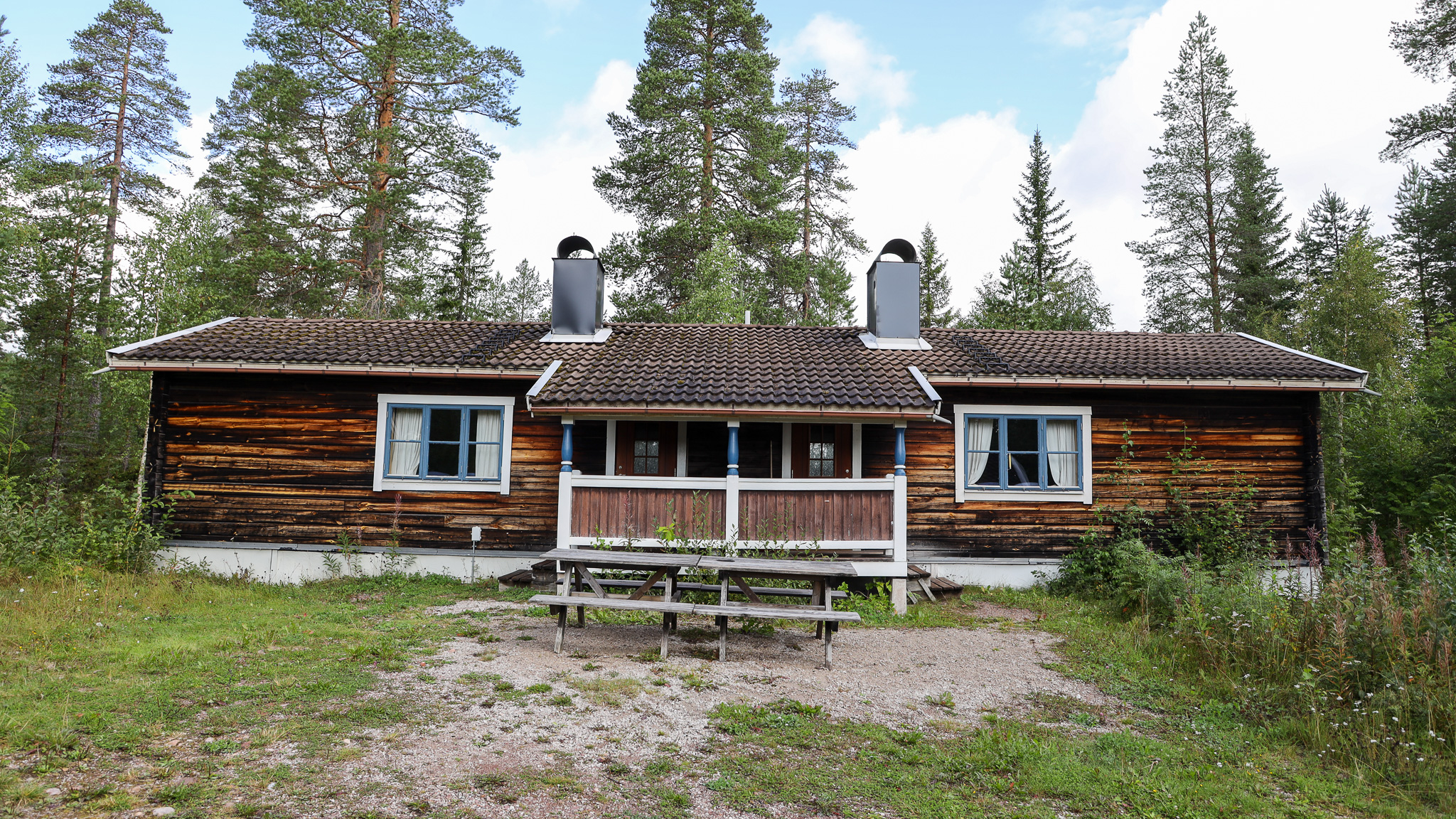 Trästuga med altan och stora fönster, omgiven av skog. Trästuga med altan och stora fönster, omgiven av skog.