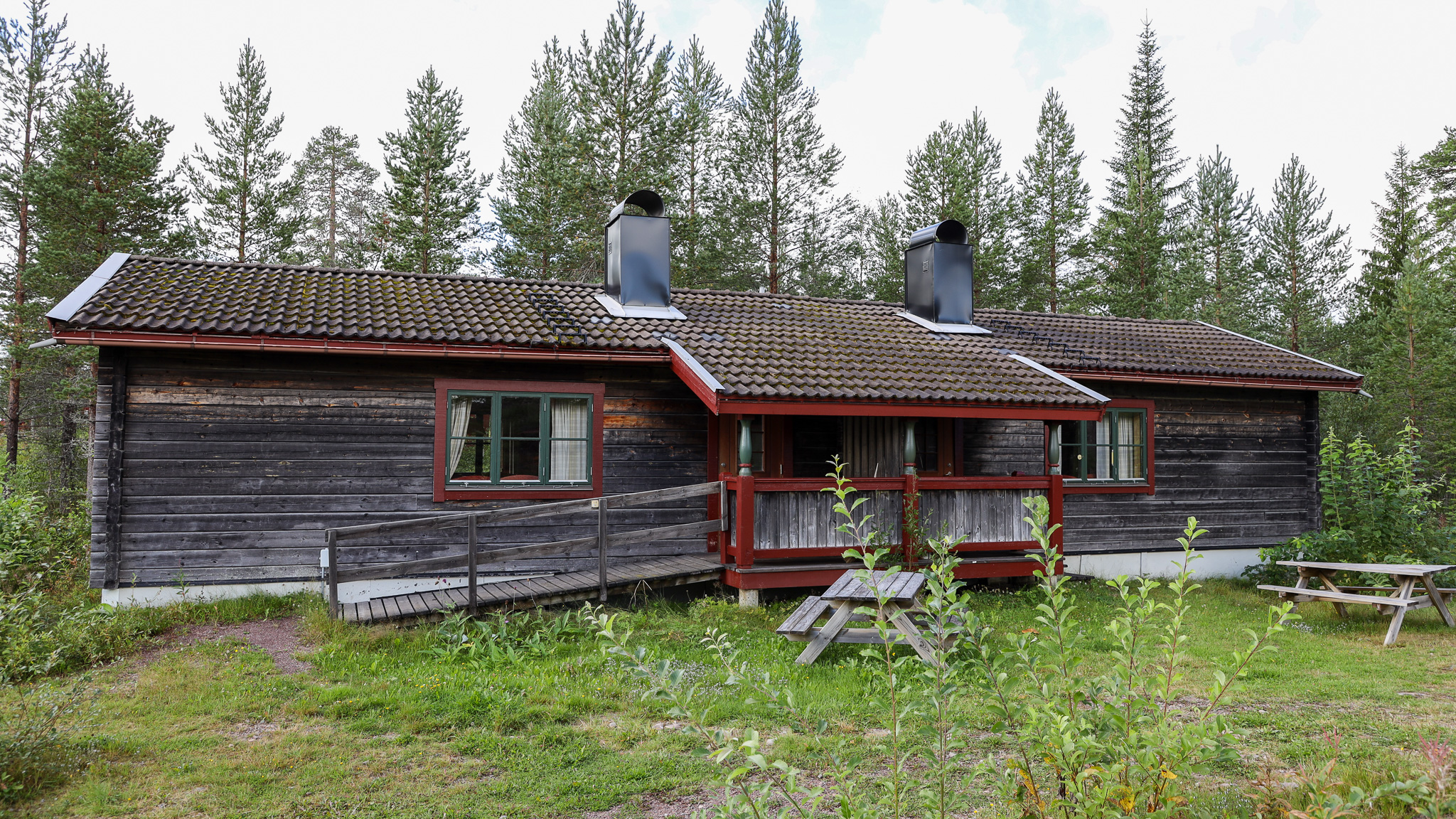 Mörk trästuga med veranda, omgiven av skog och grönska. Mörk trästuga med veranda, omgiven av skog och grönska.