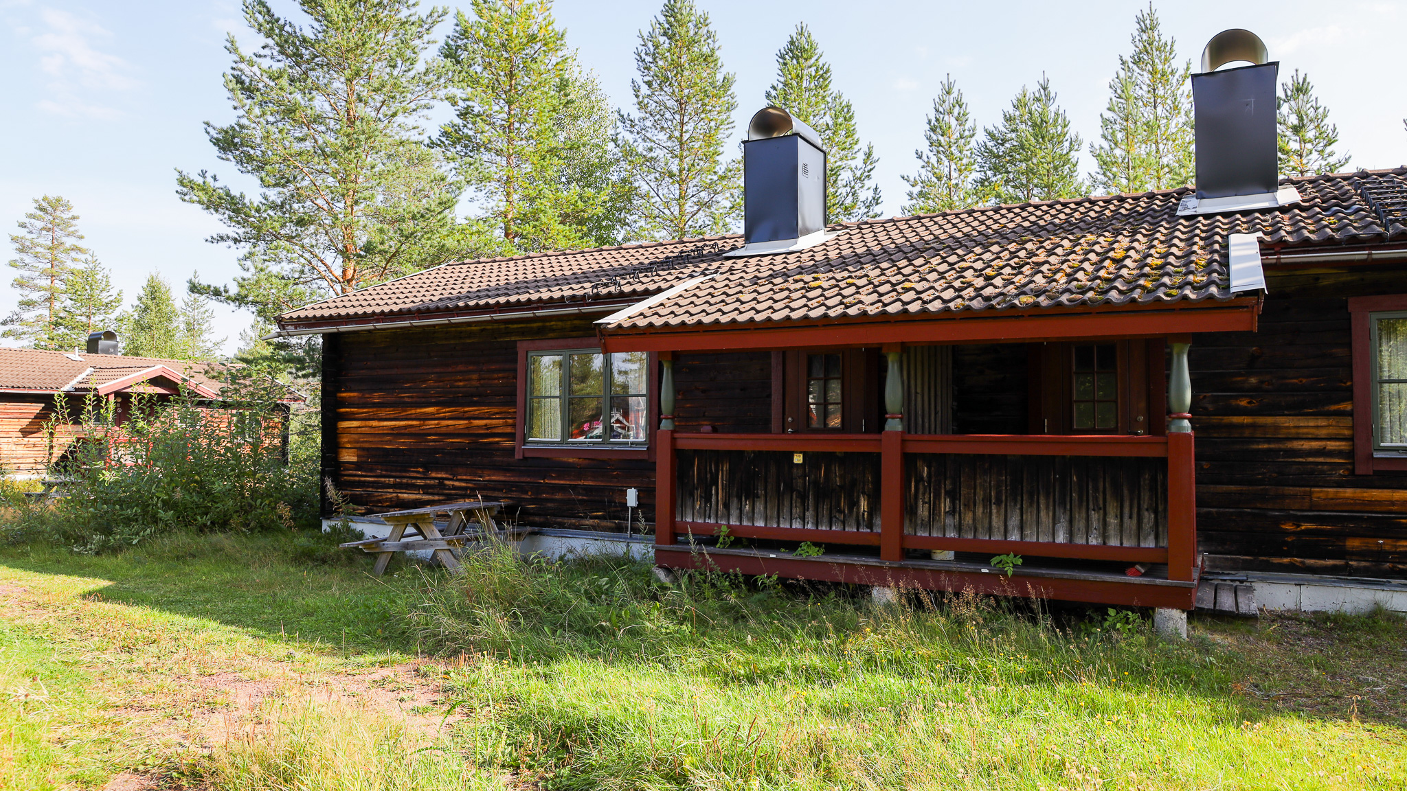 Mörk trästuga med veranda och entré, omgiven av skog. Mörk trästuga med veranda och entré, omgiven av skog.
